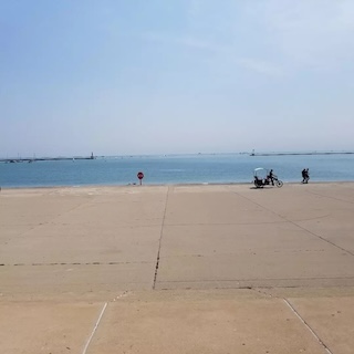 Photograph of Lake Michigan. At the bottom of the shot is a large concrete pad running along the shore. The concrete looks similar to sand. 