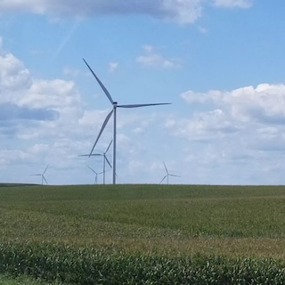 Photograph of several wind turbines in a field under a lightly cloudy sky. 